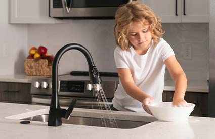 Child washes dishes in kitchen sink designed by R.J. Parins Green Bay Wisconsin plumbing and heating kitchen and bath design services.